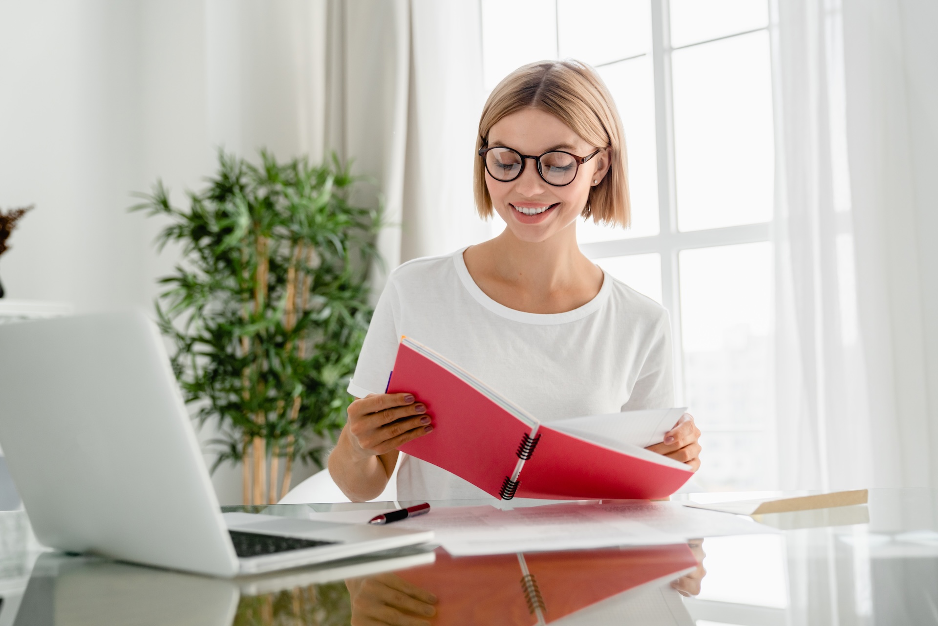Happy young caucasian woman taking notes, writing and doing e-learning using laptop at home.